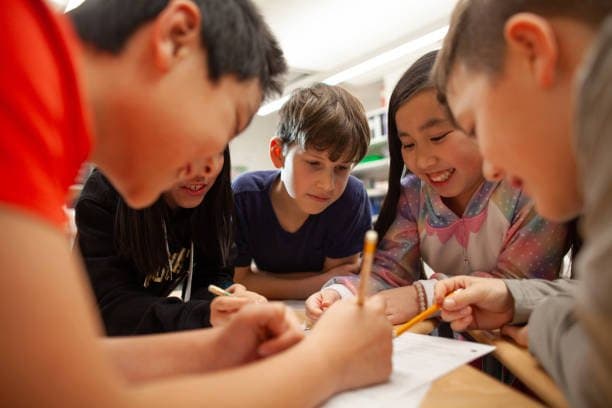 A group of students huddled around a table, working together on a worksheet with pencils.